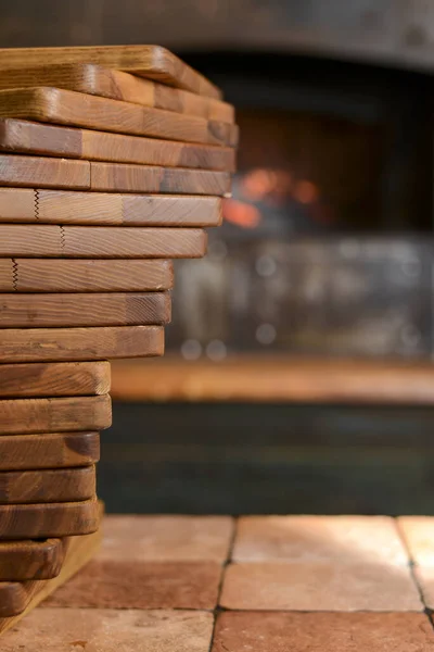 Stack of wooden cutting boards for professional cooks in a restaurant with a brick stove on the background. Copy space.