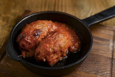 Stuffed cabbage leaves with minced meat and rice in tomato sauce on in a pan on wooden table. Lazy cabbage rolls.