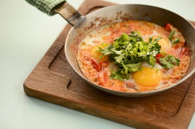 A freshly baked egg, tomato and green pepper frittata in a pan on wooden cutting board with blue mint background.