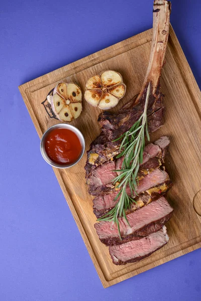 Sliced grilled Medium rare barbecue Steak on bone with spices served on a rustic wooden board over blue background.