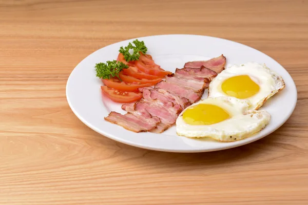 Petit déjeuner avec bacon, oeuf frit et tomates servi sur assiette blanche sur table en bois rustique léger . — Photo