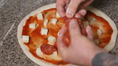 Üniformalı fırıncının elleri pizzaya pepperoni ekliyor. Pizza Sanatı. Pizza yapma süreci..