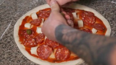 Üniformalı fırıncının elleri pizzaya pepperoni ekliyor. Pizza Sanatı. Pizza yapma süreci..