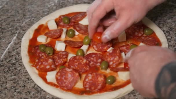 Manos de cocinero panadero en uniforme añadiendo pepperoni en la pizza. Arte de Pizza. El proceso de hacer pizza . — Vídeo de stock