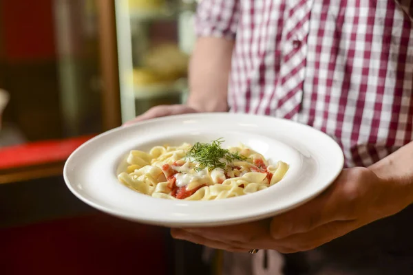Bir garson lezzetli bir tabak yemek tutar. İtalyan mutfağı, soslu makarna ve parmesan peyniri..