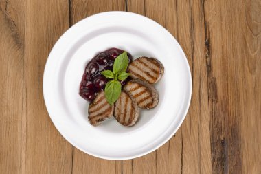 Koyu ahşap arka planda beyaz bir tabakta servis edilen ızgara et parçaları. İtalyan mutfağı.