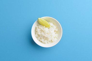 Küçük beyaz bir kasede servis edilen limonlu beyaz pirinç. Parlak mavi arkaplanda izole edilmiş.