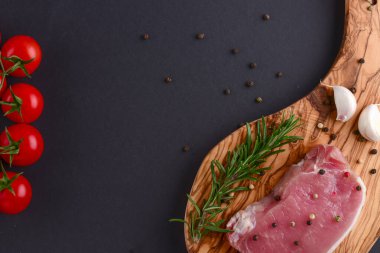 Taze çiğ biftek ahşap kesim tahtasında siyah arka planda baharatlarla, üst manzara.