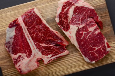 Fresh raw beef steak on wooden cutting board, top view. Served over black background.