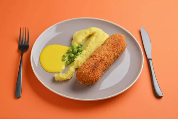 Cordon bleu cutlet, friterat kött serveras med potatismos och gröna ärtor på grå platta över orange bakgrund. — Stockfoto