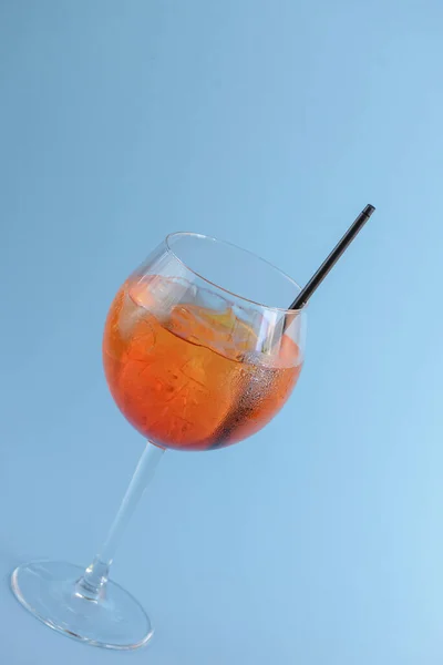Cold summer alcohol cocktail with ice and orange in a wine glass and black plastic straw on light pastel blue background — Stockfoto