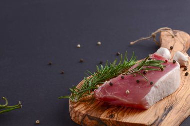 Taze çiğ biftek ahşap kesim tahtasında siyah arka planda baharatlarla, üst manzara.