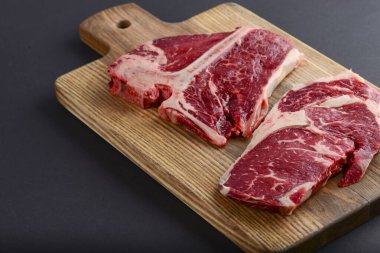 Tahta kesme tahtasında taze çiğ biftek, üst manzara. Biftek siyah arka planda servis ediliyor..