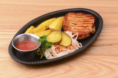 Izgara biftek, sebze ve domates sosu açık kırsal alanda siyah bir tabakta servis edilir..