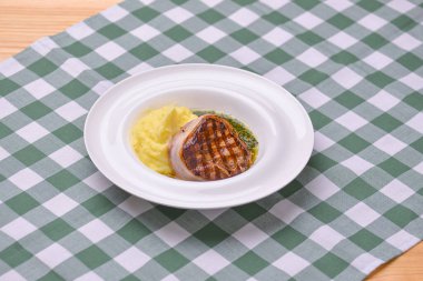 Yeşil ekose masa örtüsünün üzerinde beyaz bir tabakta servis edilen patates püresi ve pesto soslu fileminyon. Biftek..
