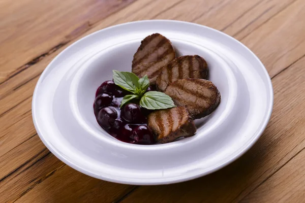Gegrilde stukjes vlees met bessensaus geserveerd op een wit bord over donkere rustieke houten achtergrond. Italiaanse keuken. — Stockfoto