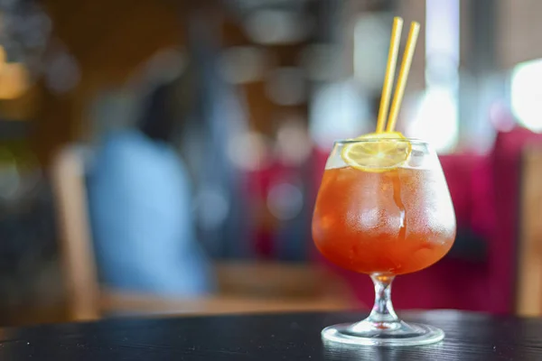 Cocktail freddo estivo con ghiaccio e limone in un piccolo bicchiere su un tavolo di legno su sfondo sfocato del ristorante . — Foto Stock