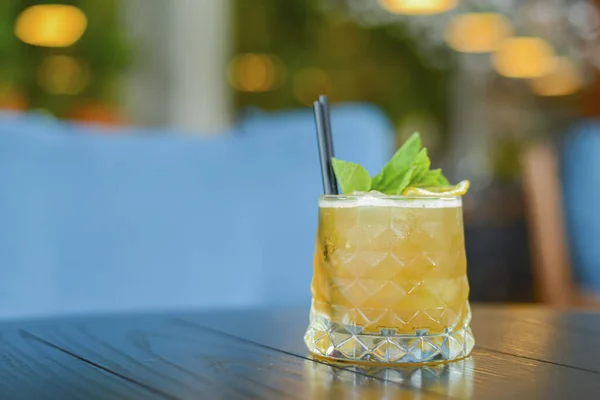 Koude zomer alcohol cocktail met ijs en citroen in een klein glas op houten tafel op wazig restaurant achtergrond. — Stockfoto