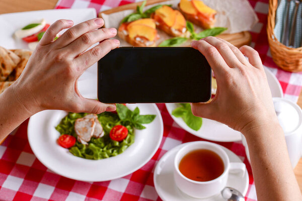 Женщина держит мобильный телефон поверх различных традиционных итальянских блюд и десертов на столе
.