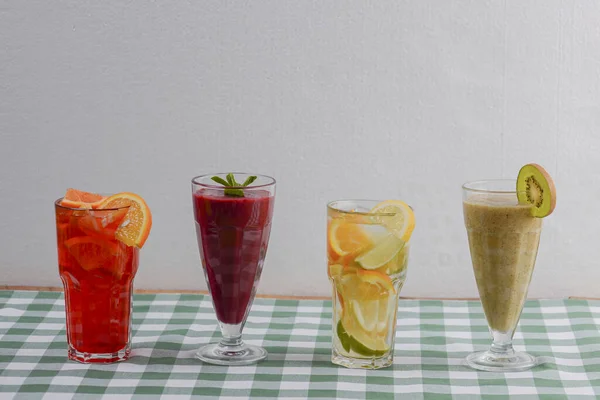 Vier tropische gemengde dranken, bessen, sinaasappel- en kiwi-fruitcocktails geserveerd op groen geruit tafelkleed. — Stockfoto