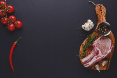 Taze çiğ biftek ahşap kesim tahtasında siyah arka planda baharatlarla, üst manzara.