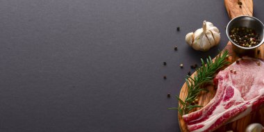 Taze çiğ biftek ahşap kesim tahtasında siyah arka planda baharatlarla, üst manzara.