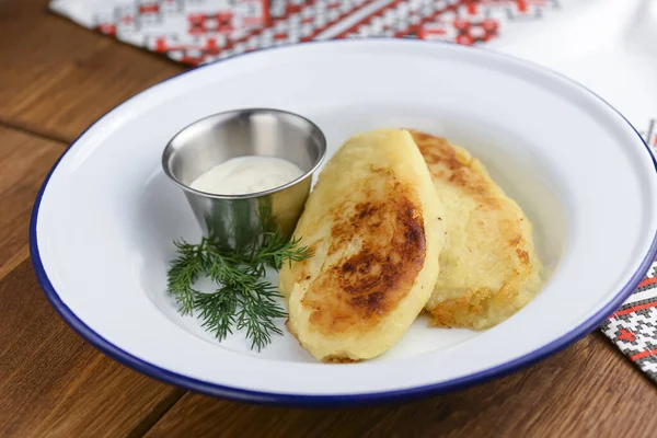 Närbild av nystekt potatis pannkakor med gräddfil i vit platta över rustika trä bord bakgrund. — Stockfoto