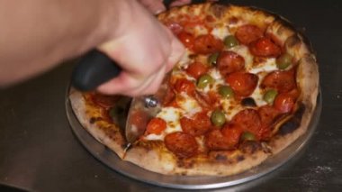 Biberli pizzayı pizza kesicisiyle dilimleyen birinin yavaş çekim yakın çekimi.