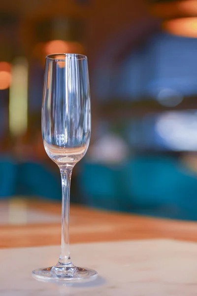Átlátszó üres pezsgőpohár a rusztikus fa asztalon homályos éttermi háttér felett. — Stock Fotó