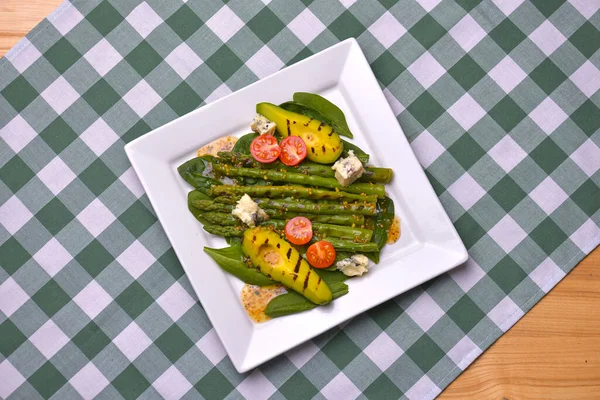 Healthy grilled avocado and asparagus salad with linen seeds and tomatoes. Served on a white square plate.