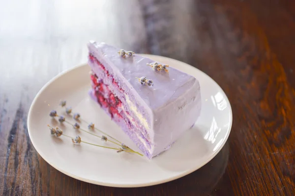 Fatia de bolo de lavanda roxa com bagas servidas com flores de lavanda em um prato branco . — Fotografia de Stock