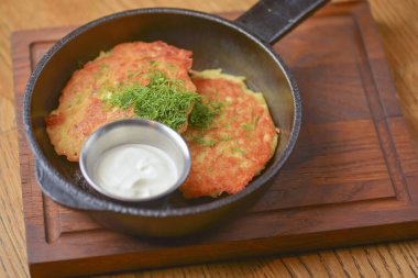 Ekşi kremalı patatesli gözlemeler ahşap bir tavada, açık sade ahşap masanın üzerinde servis ediliyor..