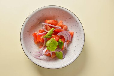 Kırmızı soğanlı taze salata, domates ve fesleğen. Parlak arka planda beyaz bir kasede servis edilmiş..