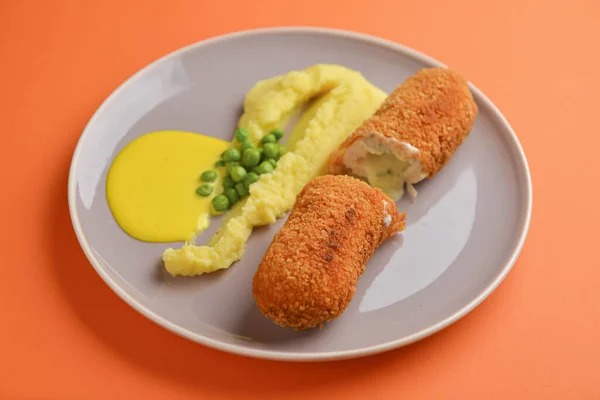 Costeleta de cordão bleu, carne frita servida com purê de batatas e ervilhas verdes na placa cinza sobre fundo laranja . — Fotografia de Stock