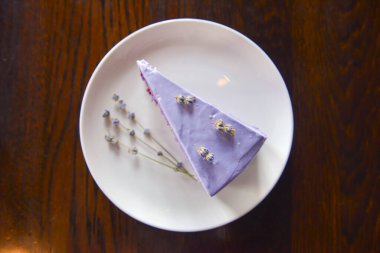 Beyaz bir tabakta lavanta çiçekleriyle servis edilen mor lavantalı kek dilimi..