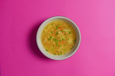 Parlak pembe arka planda izole edilmiş bir kasede servis edilen yumurtalı sebze çorbası..