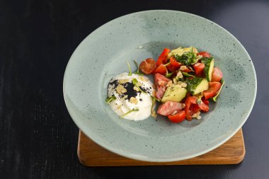 Taze sebze ve yeşil salata, siyah ahşap masa üzerinde mavi bir tabakta servis edilir..