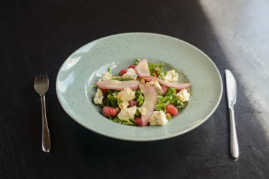 Taze sebze ve yeşil meyve salatası siyah ahşap masa üzerinde mavi bir tabakta servis edilir..