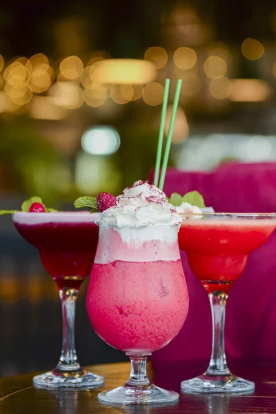 Cold summer alcohol cocktail with ice and fruit in a tall glass on light blurred restaurant or cafe background.