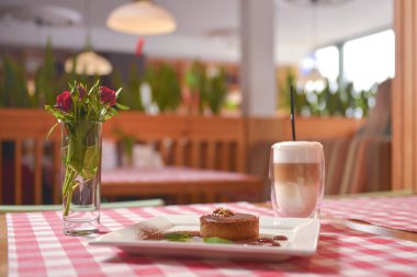 Bir parça kremalı çikolatalı pasta kakao tozu ve naneli kahve ile servis edilen kırmızı ekose masa örtüsü..