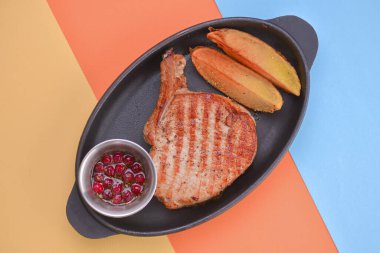 Fırında patates ve kızılcık sosuyla servis edilen pirzola bifteği siyah tepside açık renkli arka planda..