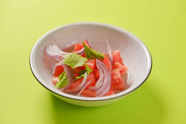 Kırmızı soğanlı taze salata, domates ve fesleğen. Parlak yeşil arka planda beyaz bir kasede servis edilmiş..