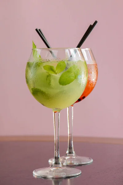 Two mojito alcohol cocktails with plastic straw, tropical beverage with ice, mint and lime on pink background copy space — Stockfoto