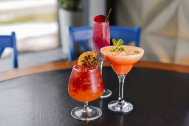 Koyu renkli ahşap bir masada servis edilen üç renkli ferahlatıcı kokteyl ve bulanık arka plan..