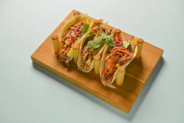 Hakiki Meksika tavuğu ve biftekli taco. Pastel mavi nane arkaplanının üzerinde ahşap bir tahtada servis edilen üç taco..