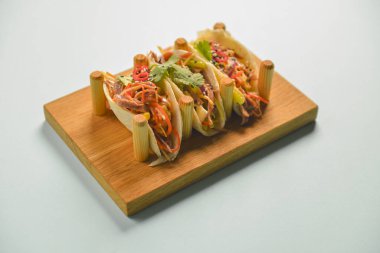 Hakiki Meksika tavuğu ve biftekli taco. Pastel mavi nane arkaplanının üzerinde ahşap bir tahtada servis edilen üç taco..