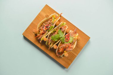 Hakiki Meksika tavuğu ve biftekli taco. Pastel mavi nane arkaplanının üzerinde ahşap bir tahtada servis edilen üç taco..