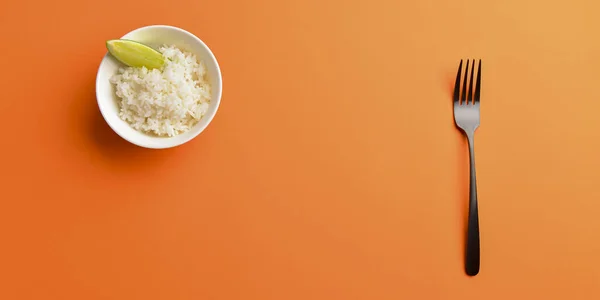 Λευκό ρύζι με ένα κομμάτι λάιμ σερβίρεται σε ένα μικρό λευκό μπολ. Απομονωμένα σε έντονο πορτοκαλί φόντο. — Φωτογραφία Αρχείου