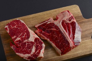 Fresh raw beef steak on wooden cutting board, top view. Served over black background.