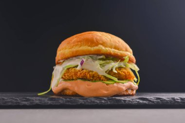 Siyah arka planda baharatlı lezzetli bir hamburgerci. Fast food, abur cubur kavramı.